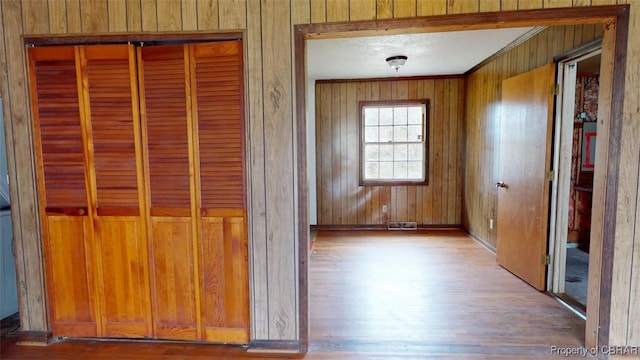 interior space with visible vents, ornamental molding, a textured ceiling, wooden walls, and wood finished floors