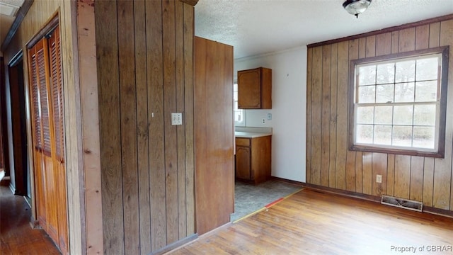 kitchen with wooden walls, visible vents, brown cabinets, wood finished floors, and light countertops