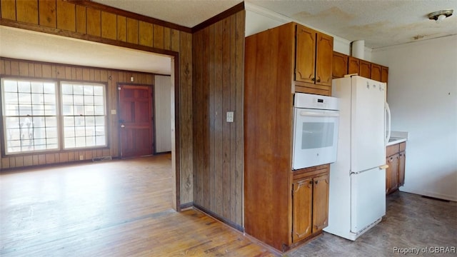 kitchen featuring brown cabinets, visible vents, light countertops, wooden walls, and white appliances