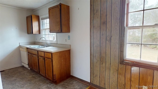 kitchen with baseboards, brown cabinetry, white dishwasher, light countertops, and a sink