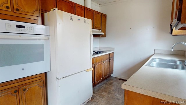 kitchen with light countertops, white appliances, a sink, and brown cabinets