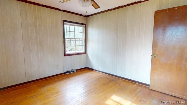 empty room featuring visible vents, light wood-style floors, ornamental molding, a ceiling fan, and baseboards