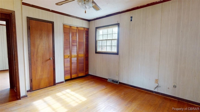 unfurnished bedroom with light wood finished floors, two closets, visible vents, and crown molding