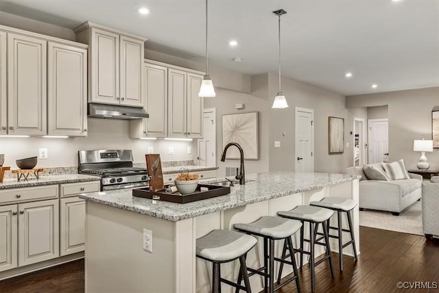 kitchen featuring stainless steel gas stove, a center island with sink, open floor plan, under cabinet range hood, and a sink