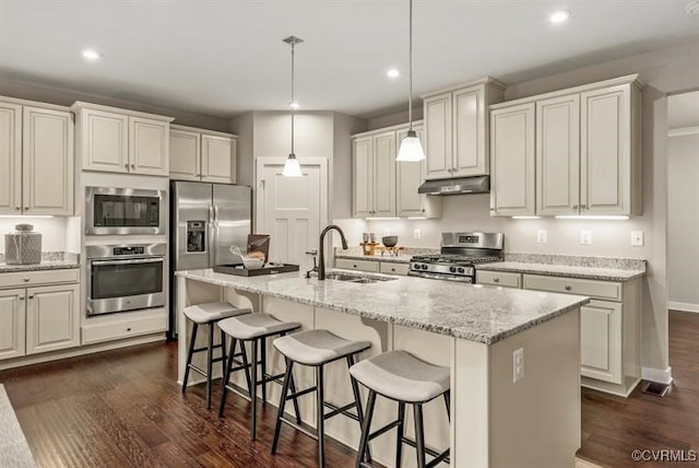 kitchen featuring pendant lighting, a center island with sink, stainless steel appliances, a sink, and under cabinet range hood