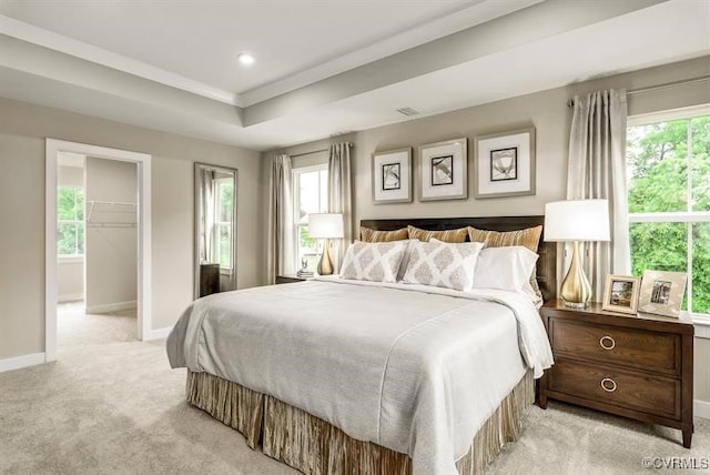 bedroom with light colored carpet, a raised ceiling, multiple windows, and baseboards