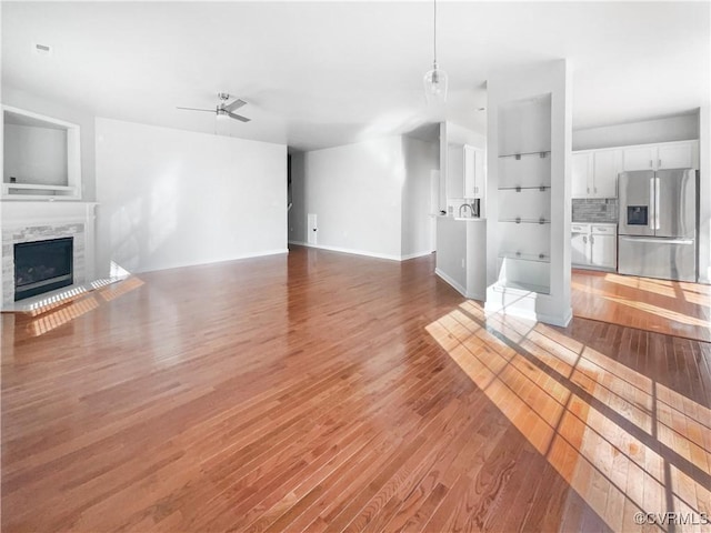 unfurnished living room featuring baseboards, wood finished floors, a ceiling fan, and a tile fireplace