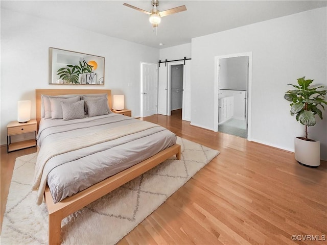 bedroom featuring a walk in closet, a barn door, a ceiling fan, connected bathroom, and light wood-type flooring