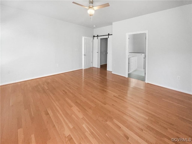 unfurnished bedroom featuring ensuite bathroom, a spacious closet, a barn door, and light wood-type flooring