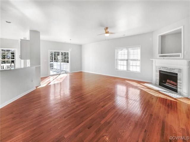 unfurnished living room featuring baseboards, a fireplace, hardwood / wood-style flooring, and a healthy amount of sunlight