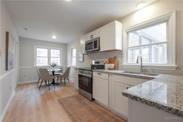 kitchen featuring appliances with stainless steel finishes, light stone counters, light wood-type flooring, white cabinetry, and a sink