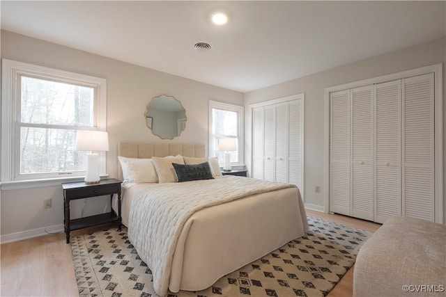 bedroom with light wood finished floors, baseboards, visible vents, and two closets