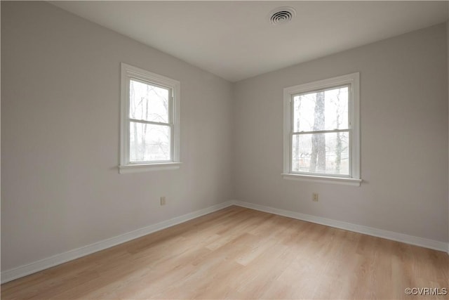 spare room featuring light wood-type flooring, visible vents, and baseboards