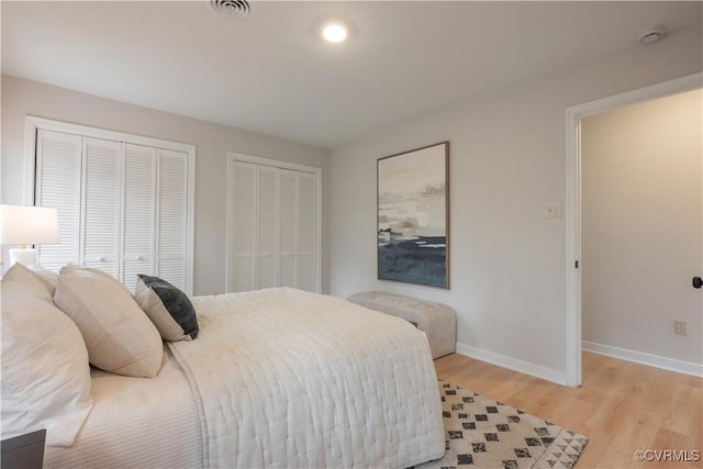 bedroom featuring light wood-type flooring, visible vents, baseboards, and two closets