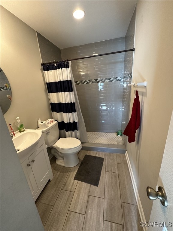 full bath with toilet, wood finish floors, vanity, baseboards, and a shower stall