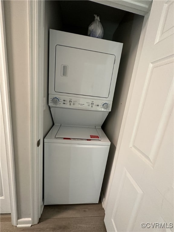 clothes washing area featuring laundry area, wood finished floors, and stacked washer and clothes dryer