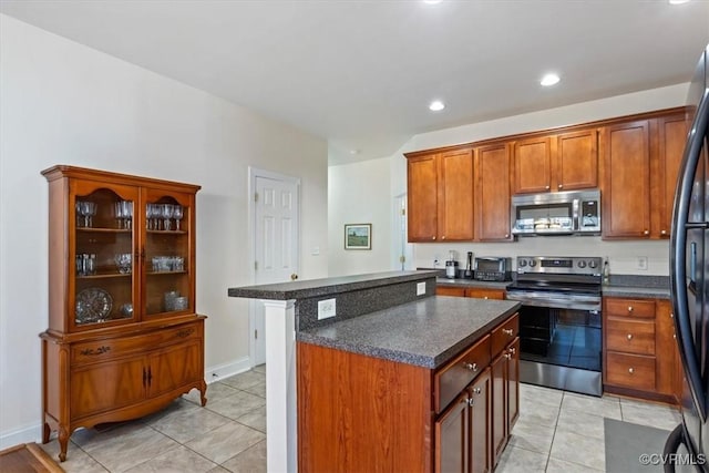 kitchen featuring appliances with stainless steel finishes, dark countertops, a kitchen island, and light tile patterned flooring