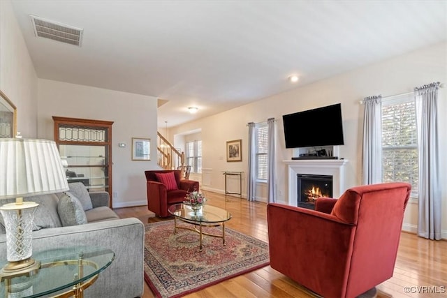 living area with a warm lit fireplace, plenty of natural light, visible vents, stairs, and light wood-type flooring