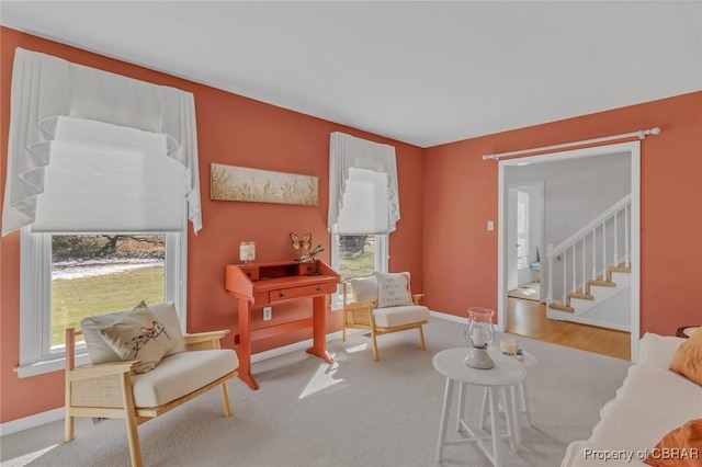 living area featuring a healthy amount of sunlight, light carpet, baseboards, and stairs