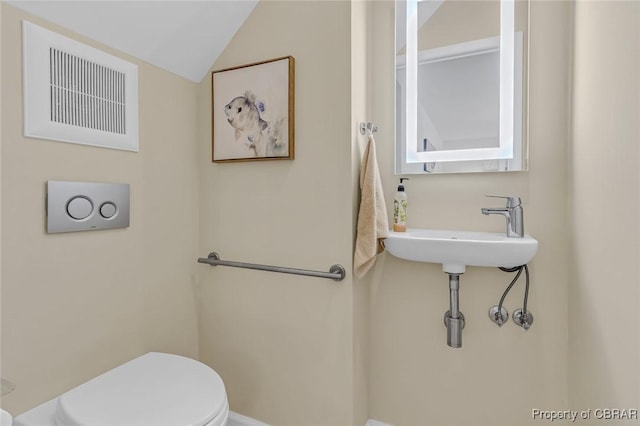 half bath with vaulted ceiling, visible vents, a sink, and toilet