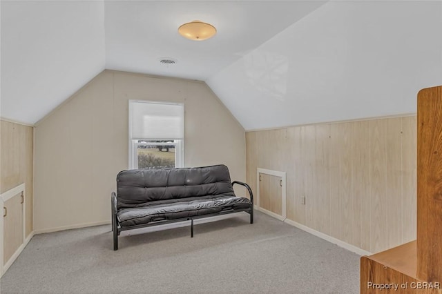 living area with baseboards, visible vents, light colored carpet, vaulted ceiling, and wood walls