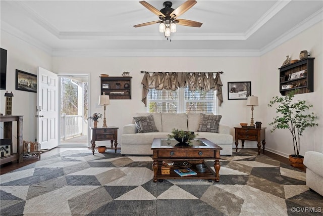 living area featuring ceiling fan, a tray ceiling, baseboards, and ornamental molding