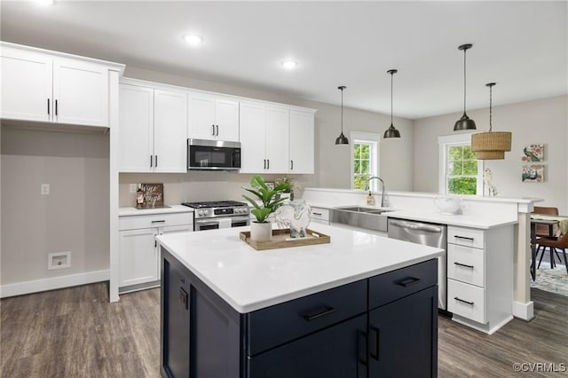 kitchen with white cabinets, light countertops, appliances with stainless steel finishes, a center island, and decorative light fixtures