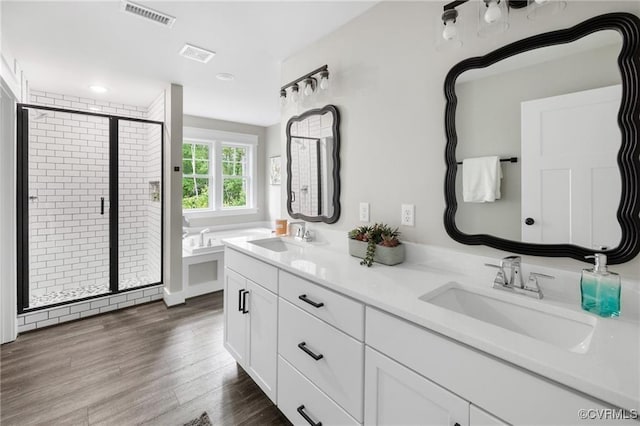 full bath with double vanity, visible vents, a sink, and wood finished floors