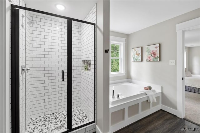 ensuite bathroom with a garden tub, wood finished floors, baseboards, a stall shower, and ensuite bath