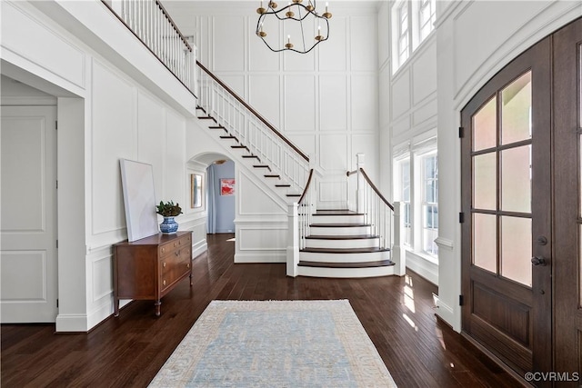 foyer featuring dark wood-style floors, arched walkways, a decorative wall, a towering ceiling, and stairs