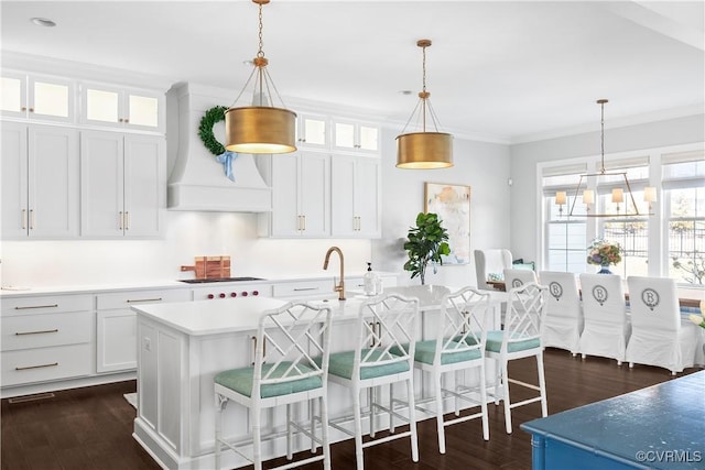 kitchen with dark wood finished floors, an island with sink, ornamental molding, light countertops, and premium range hood