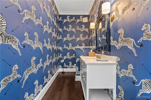 bathroom featuring wallpapered walls, baseboards, wood finished floors, crown molding, and vanity