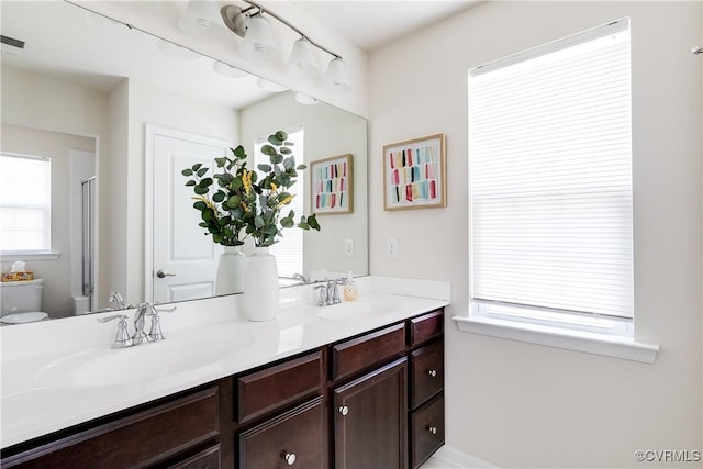 bathroom with double vanity, a shower with shower door, a sink, and toilet