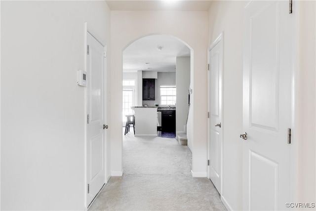 hall with baseboards, arched walkways, and light colored carpet