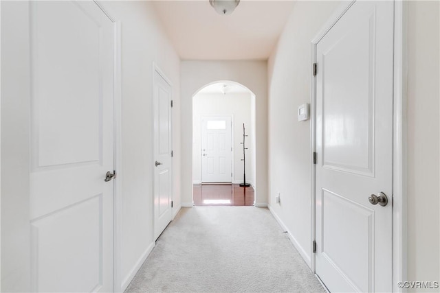 hallway featuring arched walkways, light carpet, and baseboards