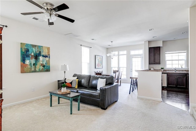 living area with light carpet, baseboards, visible vents, and ceiling fan with notable chandelier