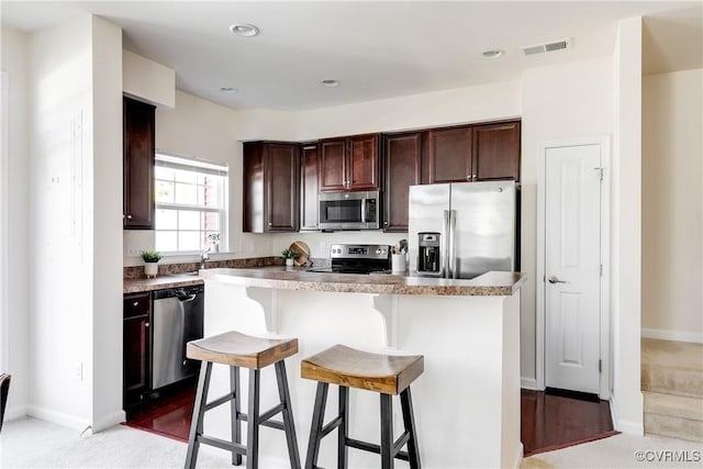 kitchen featuring visible vents, a breakfast bar, a center island, stainless steel appliances, and dark brown cabinets