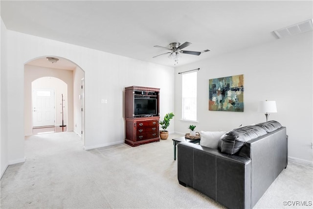 living room featuring arched walkways, light carpet, visible vents, baseboards, and a ceiling fan