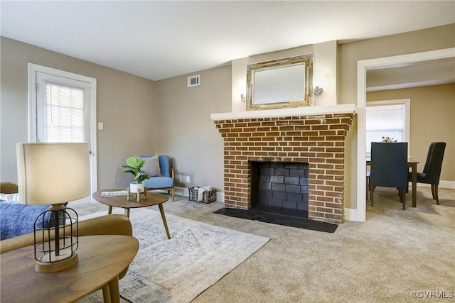 living area featuring plenty of natural light, light carpet, a fireplace, and visible vents