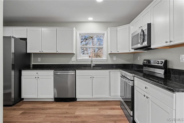 kitchen with light wood-style flooring, a sink, white cabinets, appliances with stainless steel finishes, and dark stone counters