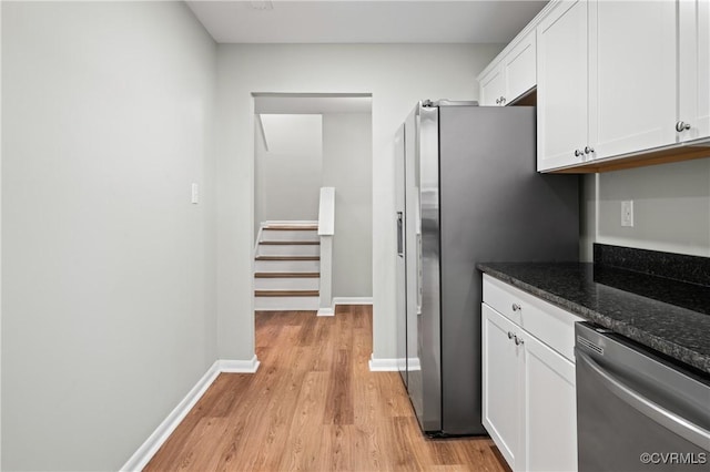 kitchen featuring baseboards, dark stone counters, light wood-style flooring, white cabinetry, and stainless steel dishwasher