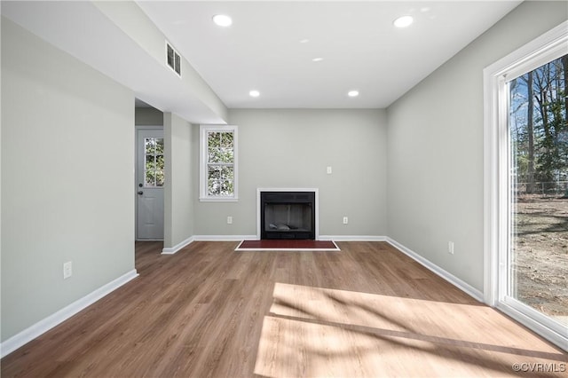 unfurnished living room featuring recessed lighting, visible vents, light wood-style flooring, a fireplace with flush hearth, and baseboards