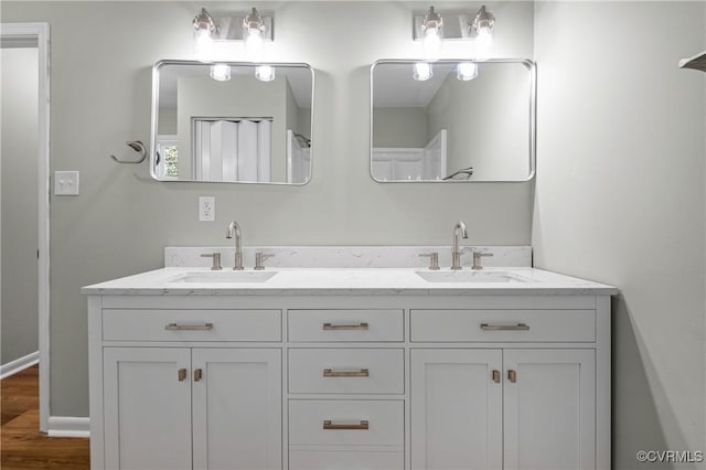 full bath with double vanity, wood finished floors, a sink, and baseboards