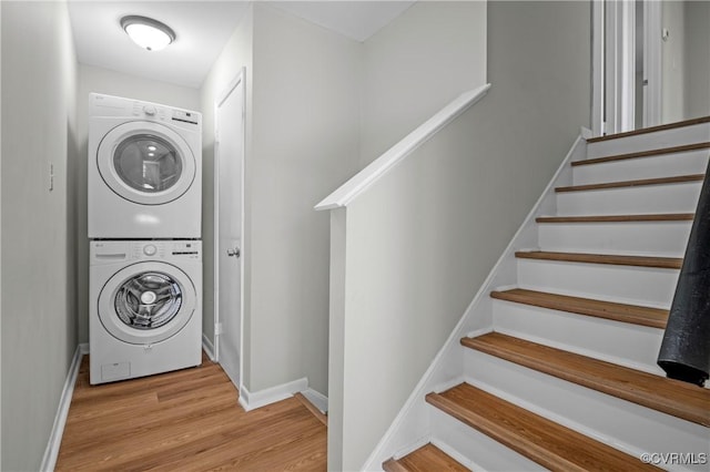 laundry area with laundry area, light wood-style flooring, baseboards, and stacked washer / drying machine