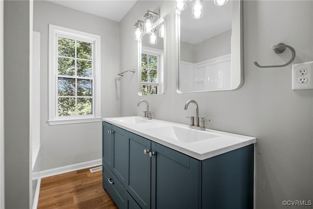 full bath featuring double vanity, baseboards, a sink, and wood finished floors