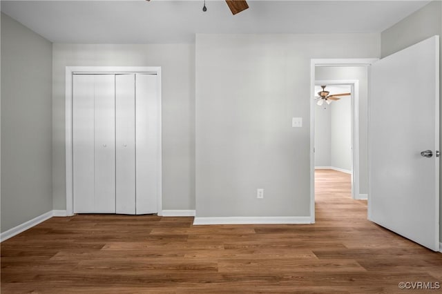 unfurnished bedroom featuring ceiling fan, a closet, baseboards, and wood finished floors