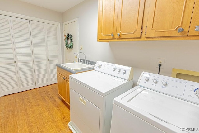 clothes washing area featuring a sink, cabinet space, light wood-style floors, and washer and dryer