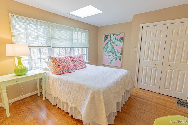 bedroom with visible vents, baseboards, light wood-type flooring, a skylight, and a closet