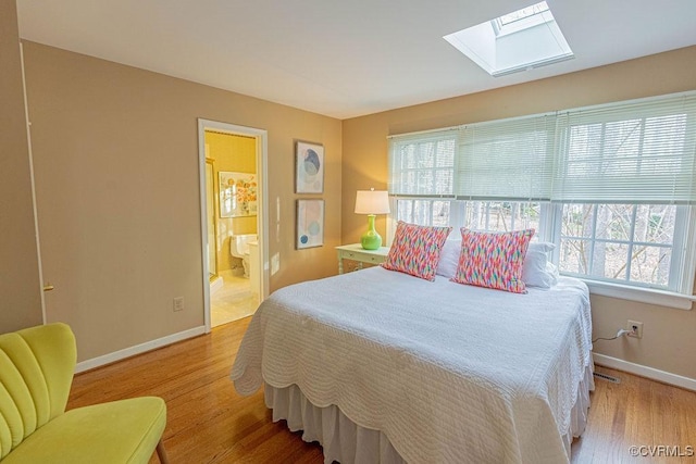 bedroom with a skylight, wood finished floors, baseboards, and connected bathroom