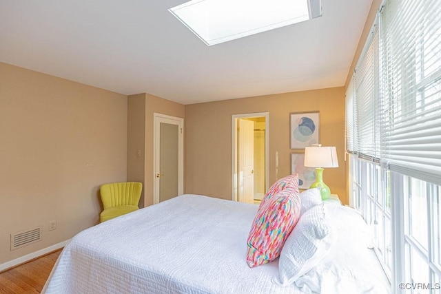 bedroom with visible vents, connected bathroom, a skylight, light wood finished floors, and baseboards